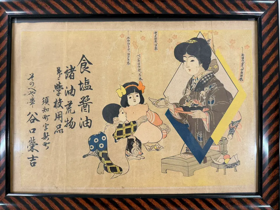 女性と子供が描かれた伝統的な木版画、上部に古い文字が記された歴史資料。谷口萬年堂の長い歴史と伝統を示す額装された古文書